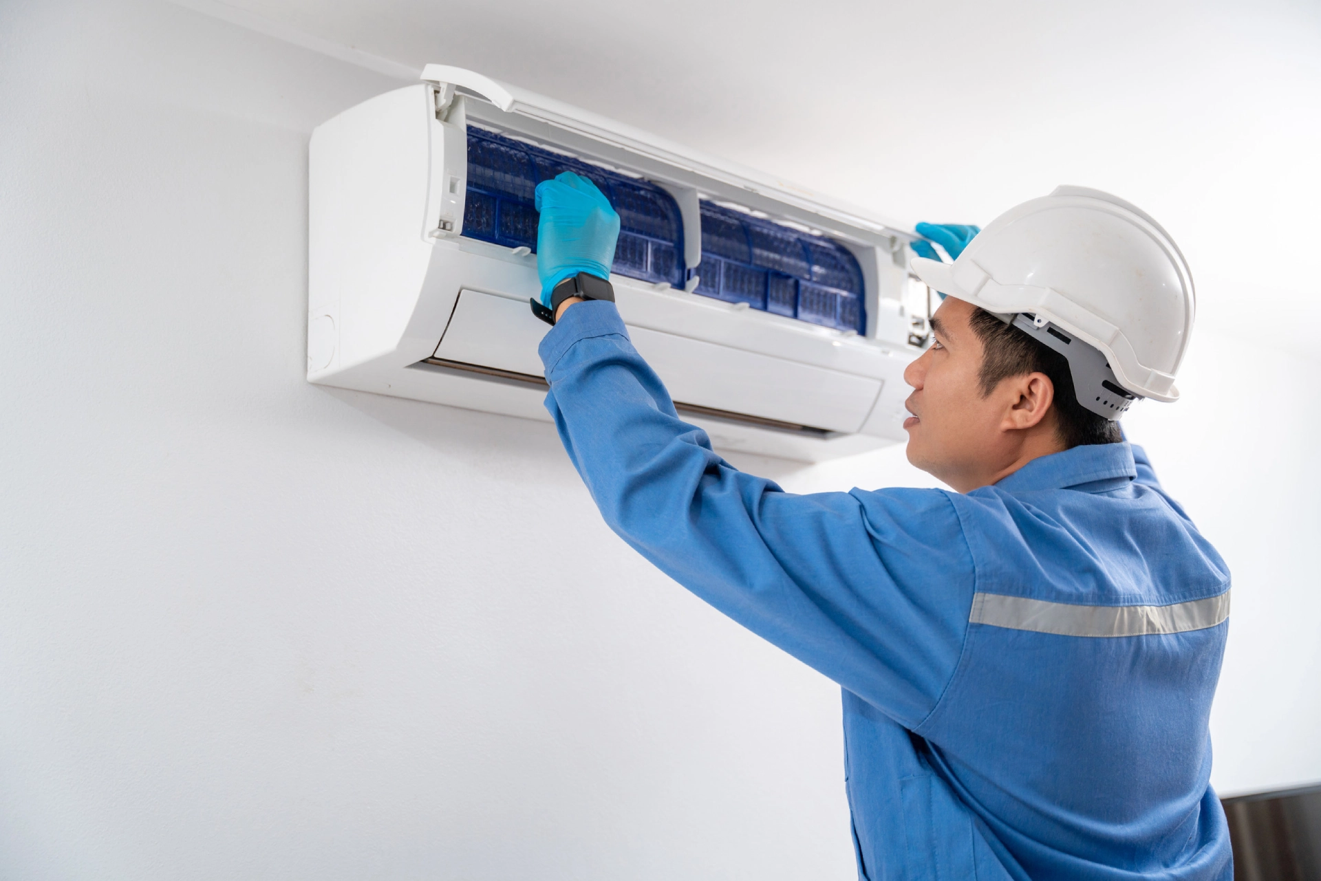 Air-technician-wearing-blue-uniform-service-checking-and-repairing-air-conditioner-on-white-wall