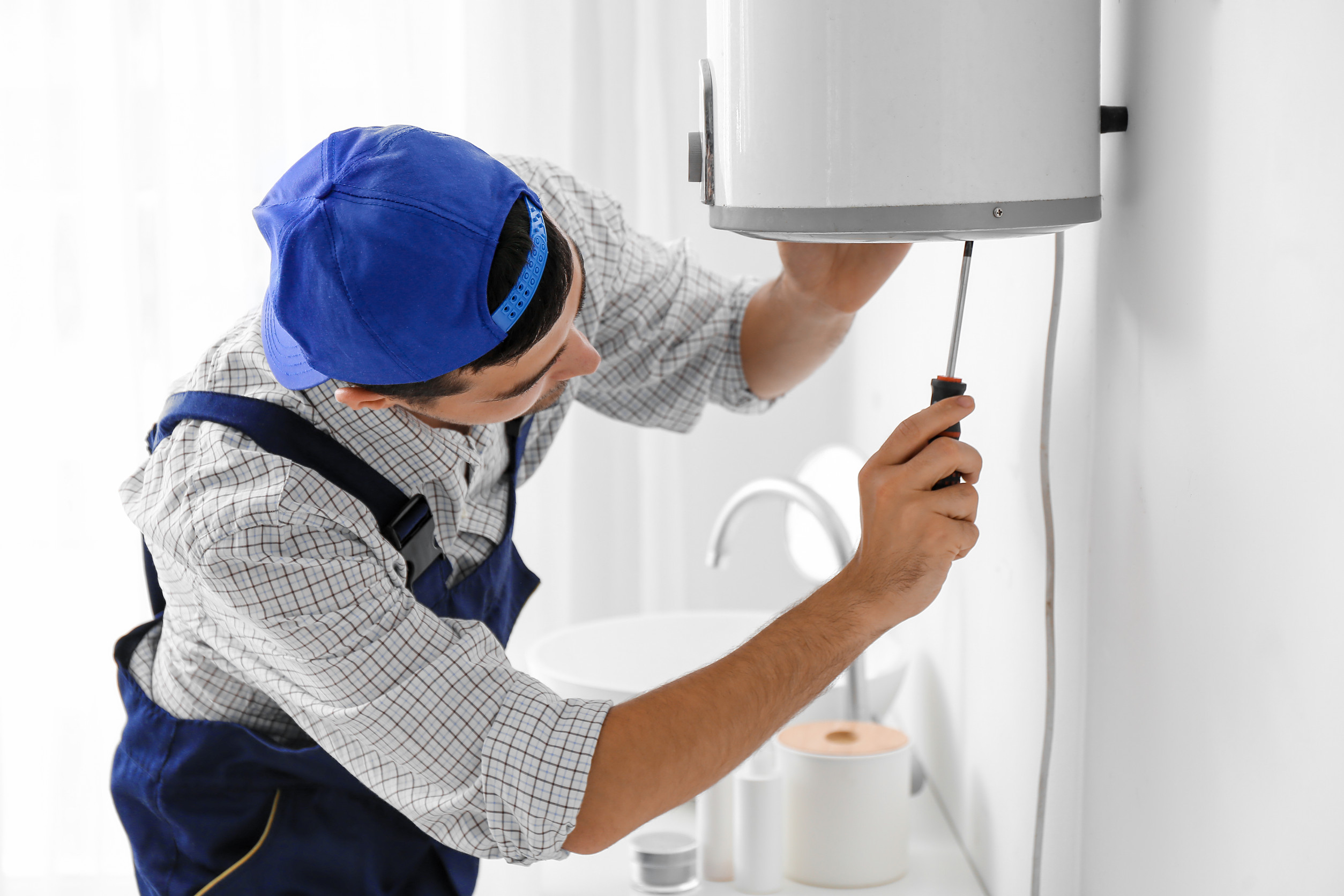 Young-plumber-repairing-boiler-with-screwdriver-in-bathroom