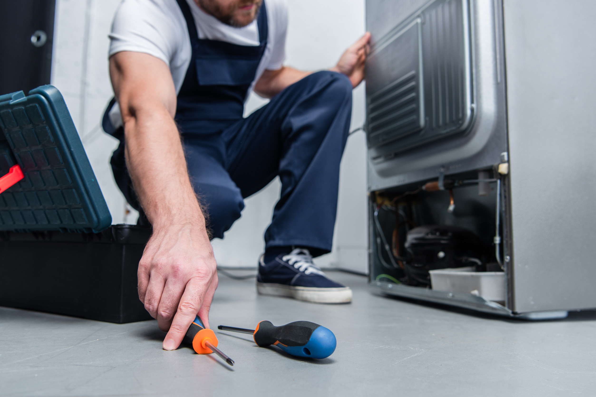 cropped-shot-of-repairman-in-working-overall-taking-screwdriver-from-floor-near-broken-refrigerator-in-kitchen